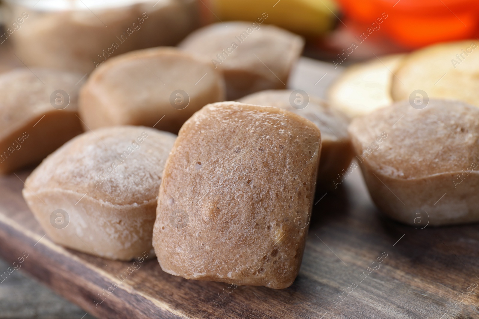 Photo of Frozen banana puree cubes on wooden board, closeup