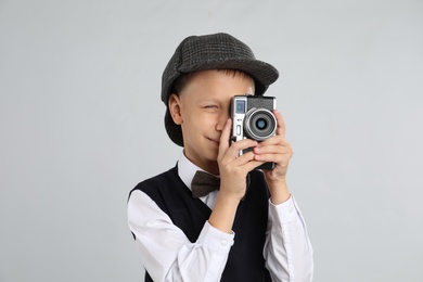 Photo of Cute little detective taking photo with vintage camera on grey background