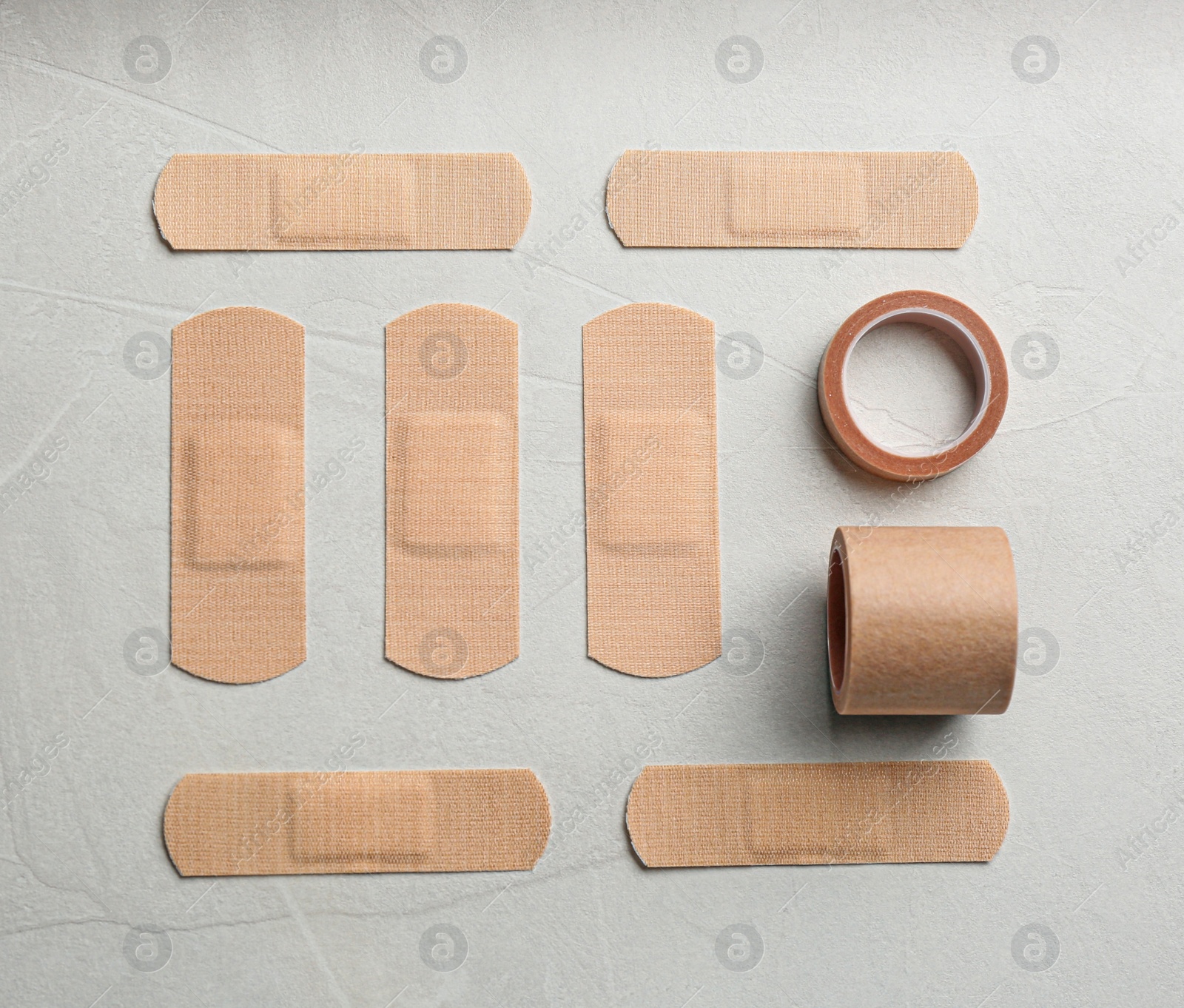 Photo of Different types of sticking plasters on light stone background, flat lay