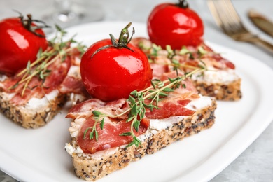 Photo of Plate of delicious bruschettas with prosciutto on grey table, closeup