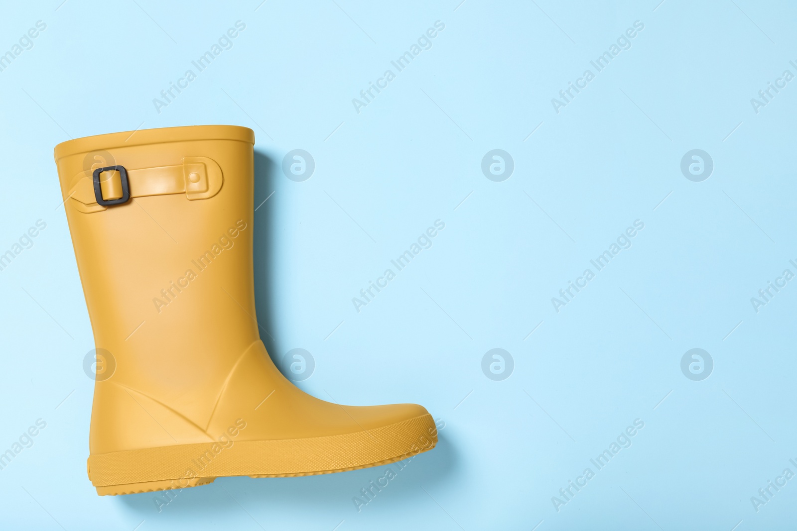 Photo of Yellow rubber boot on light blue background, top view. Space for text