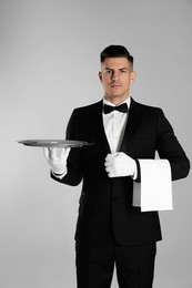 Photo of Handsome butler with tray on light grey background