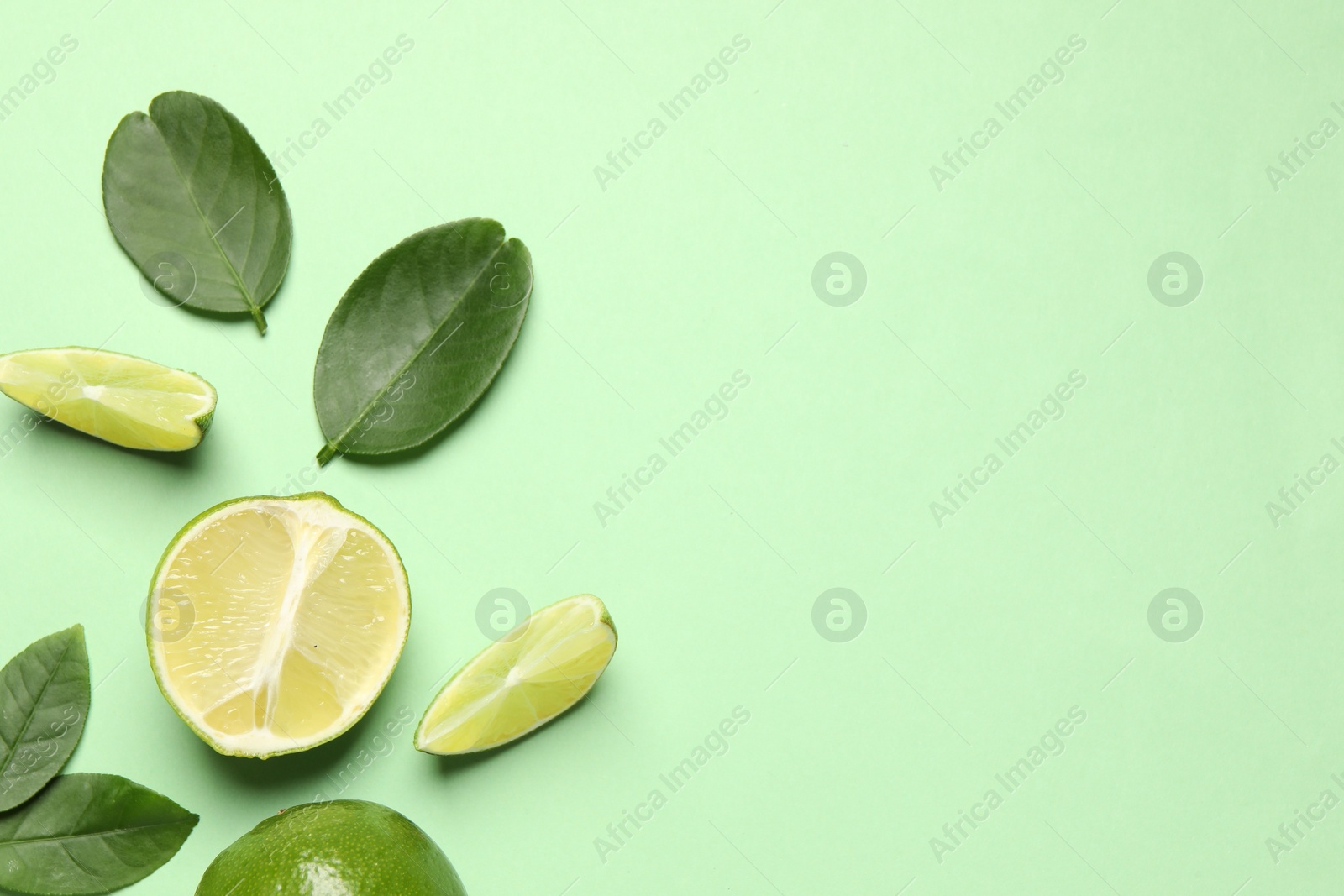 Photo of Whole and cut fresh ripe limes with leaves on light green background, flat lay