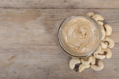 Photo of Tasty cashew nut paste in jar on wooden table, top view. Space for text