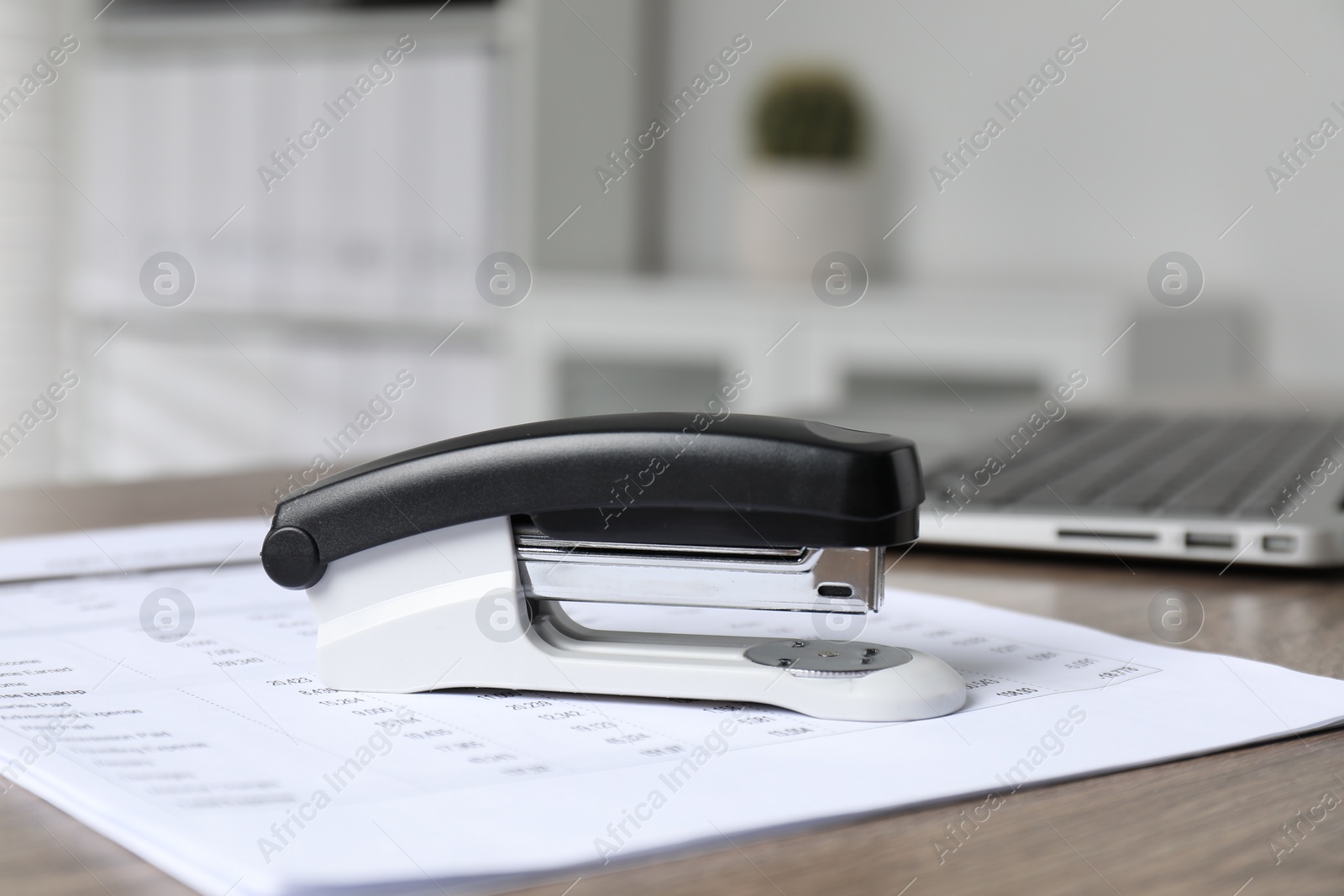 Photo of Stapler and document on wooden table indoors, closeup