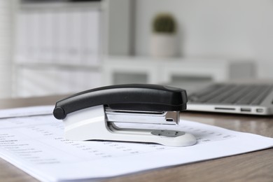 Photo of Stapler and document on wooden table indoors, closeup