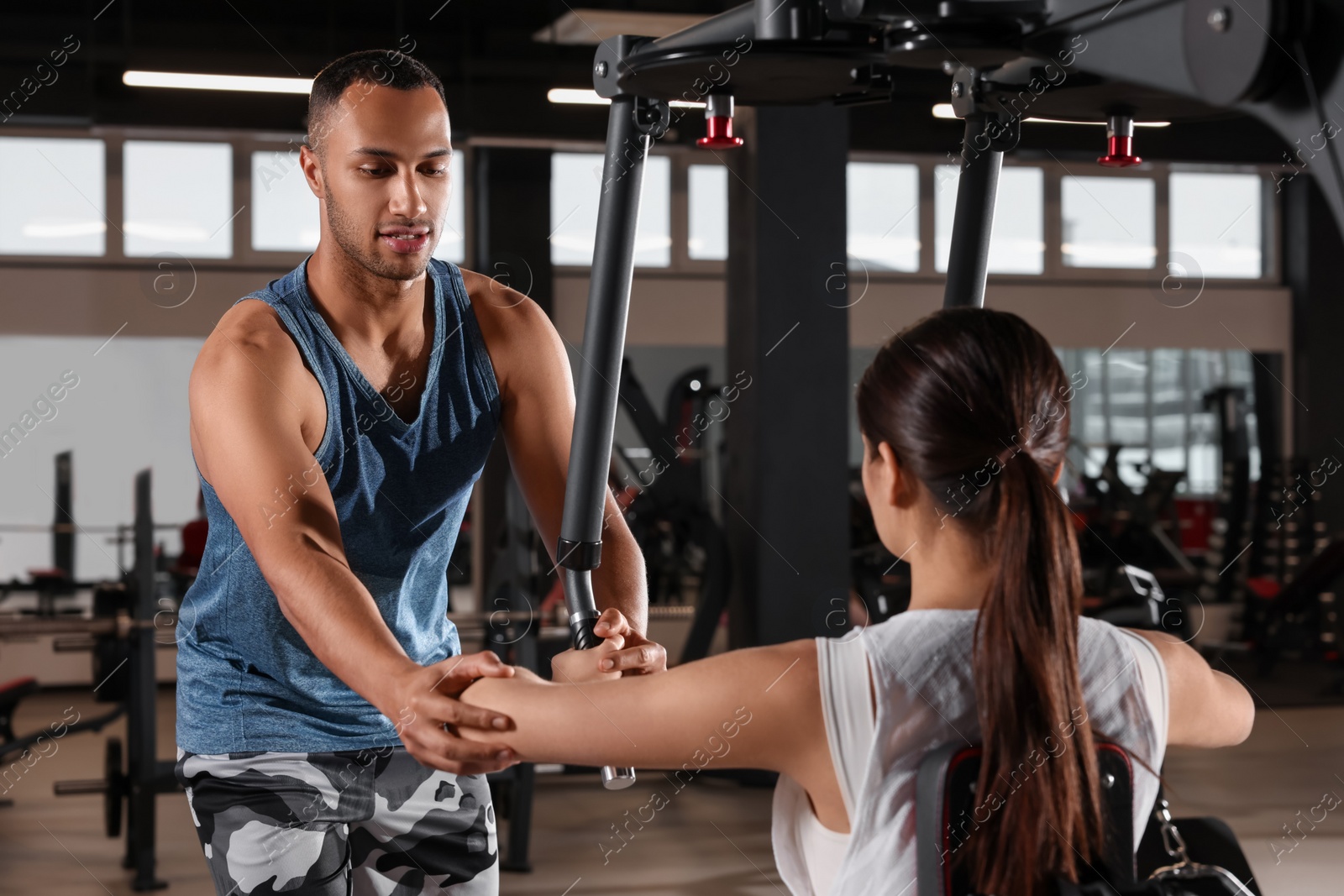 Photo of Young woman working out with professional trainer in modern gym