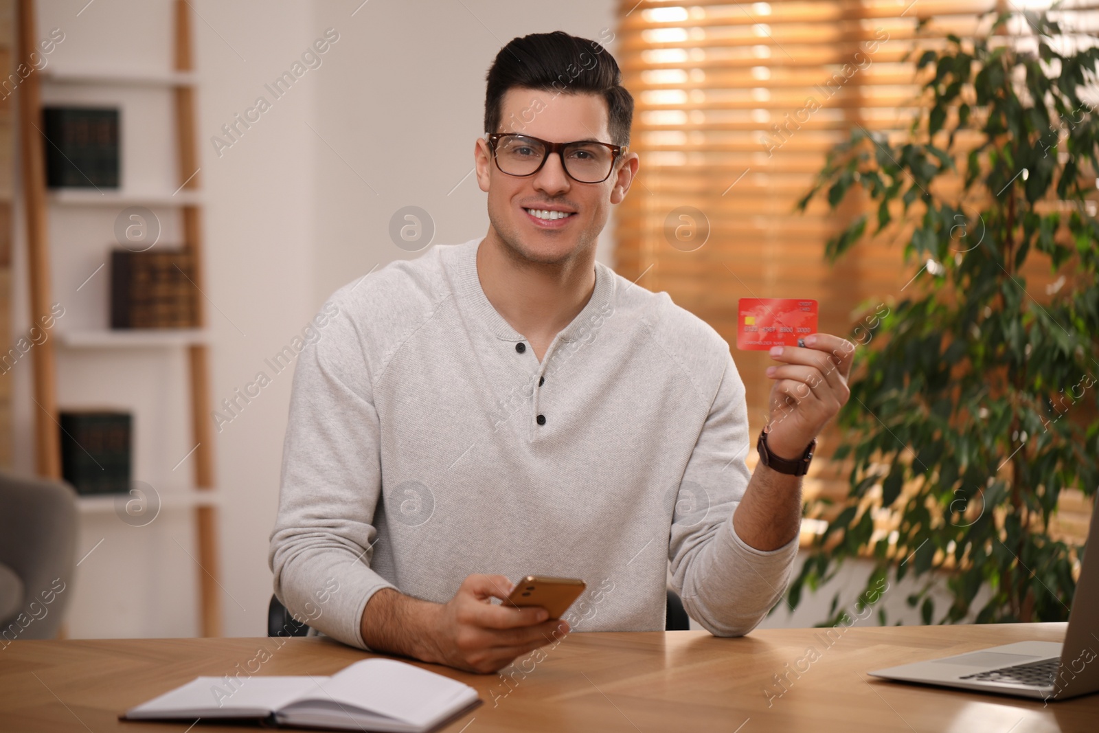 Photo of Man using smartphone and credit card for online payment at desk in room