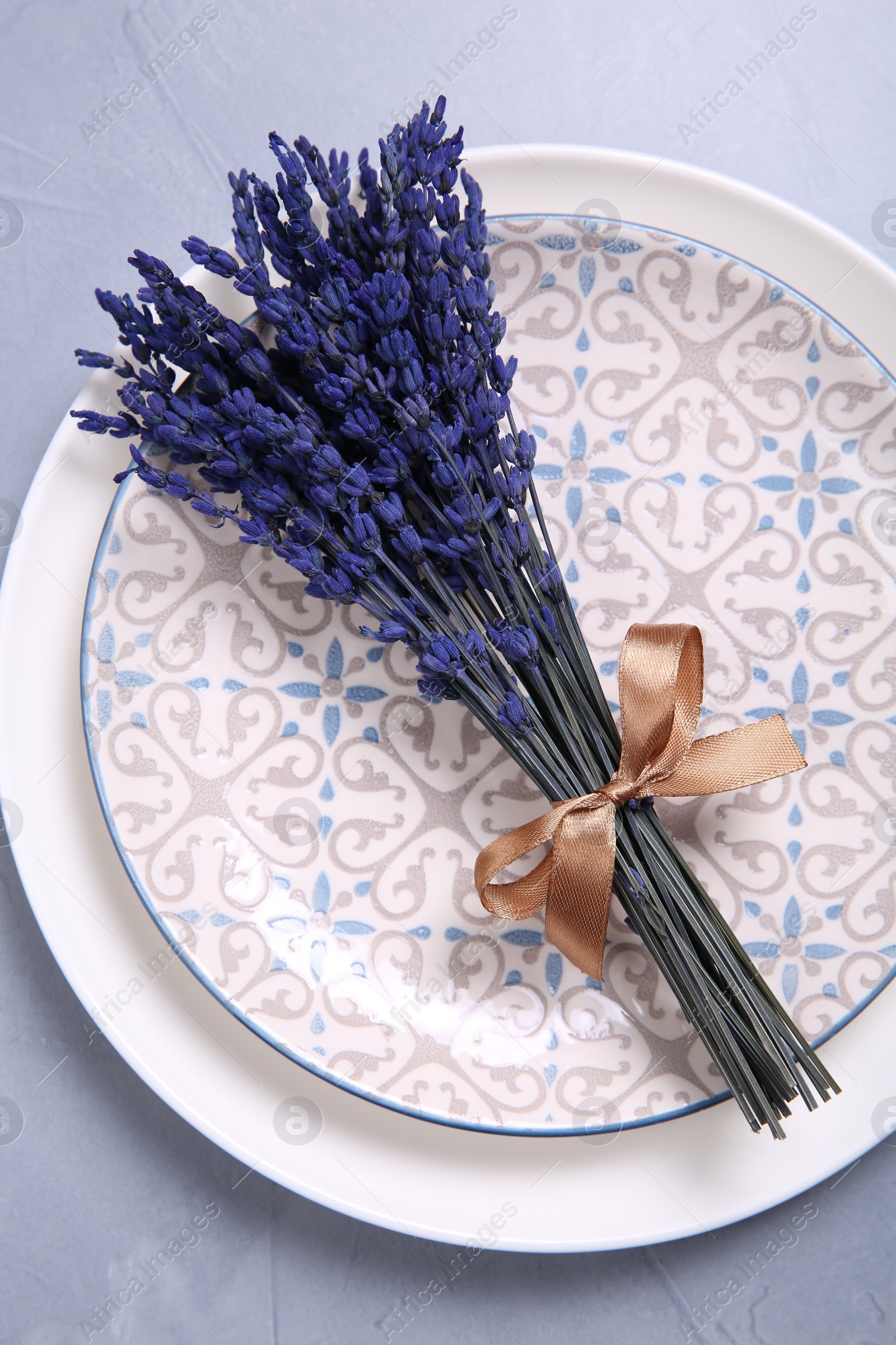 Photo of Bouquet of beautiful preserved lavender flowers and plates on light grey textured table, top view
