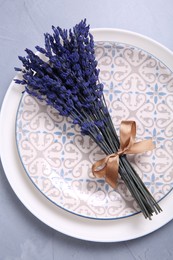 Bouquet of beautiful preserved lavender flowers and plates on light grey textured table, top view