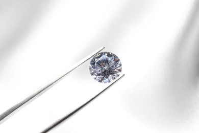 Photo of Tweezers with beautiful shiny diamond on light background, closeup