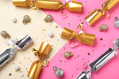 Christmas crackers with decorations and shiny confetti on color background, flat lay