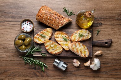 Photo of Tasty bruschettas with oil and rosemary on wooden table, flat lay