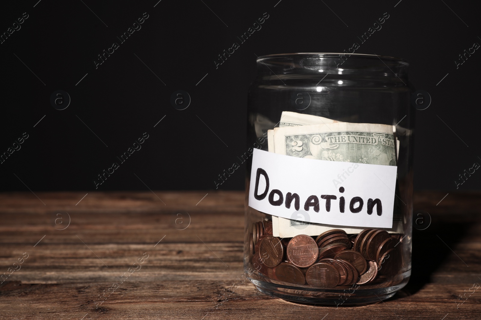 Photo of Glass jar with money and label DONATION on table against black background. Space for text