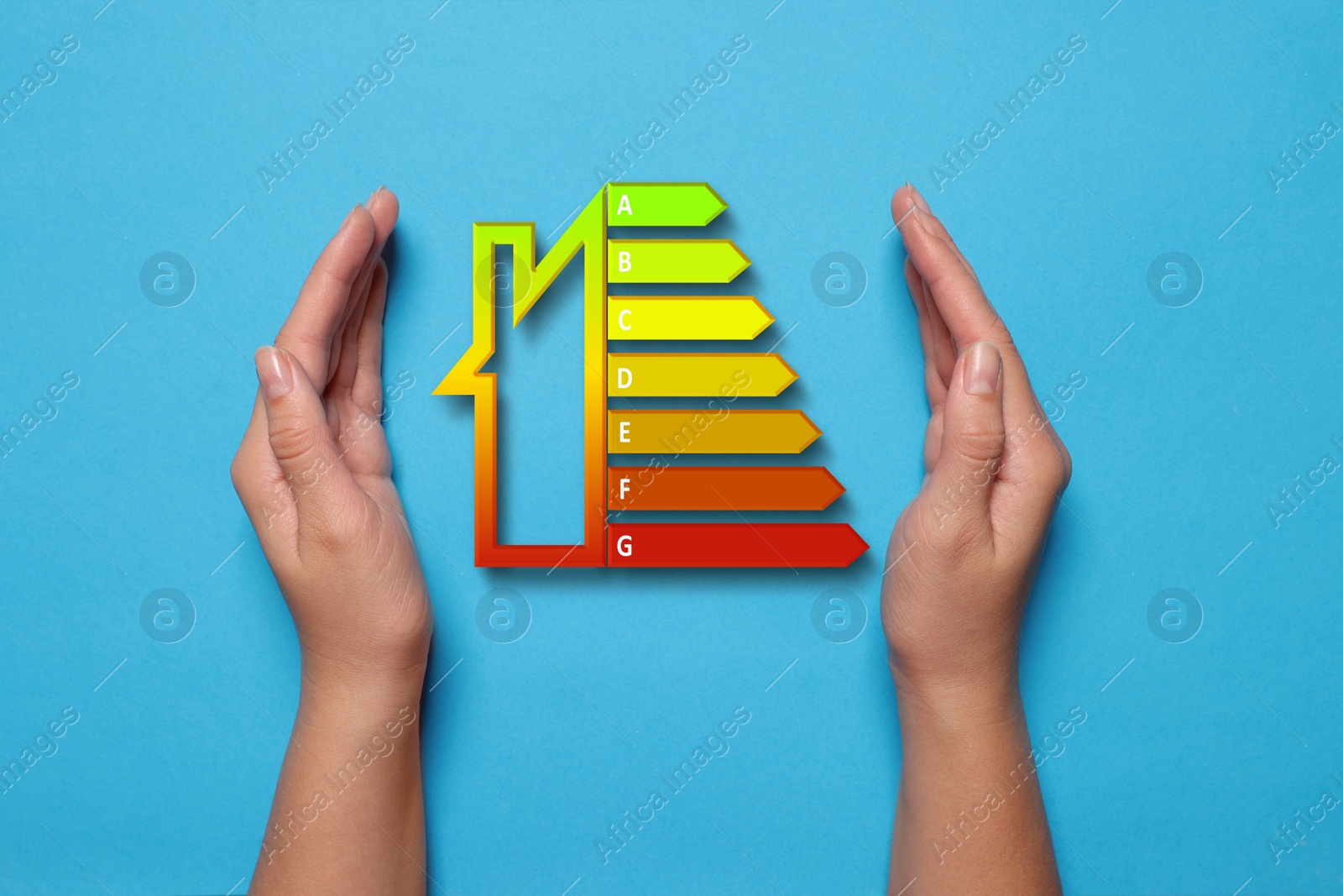 Image of Energy efficiency rating and woman holding hands near it on light blue background, top view