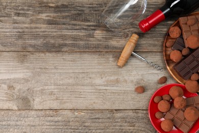 Photo of Bottle of red wine, glass, chocolate sweets and corkscrew on wooden table, flat lay. Space for text