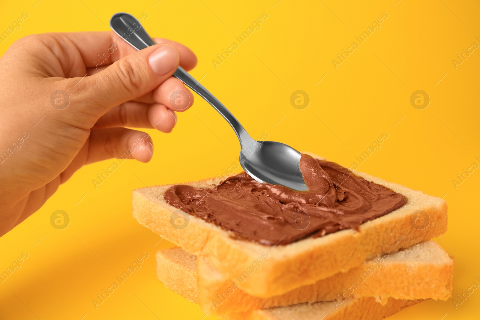 Photo of Woman spreading chocolate paste onto bread on yellow background, closeup