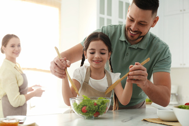 Photo of Happy family cooking salad together in kitchen