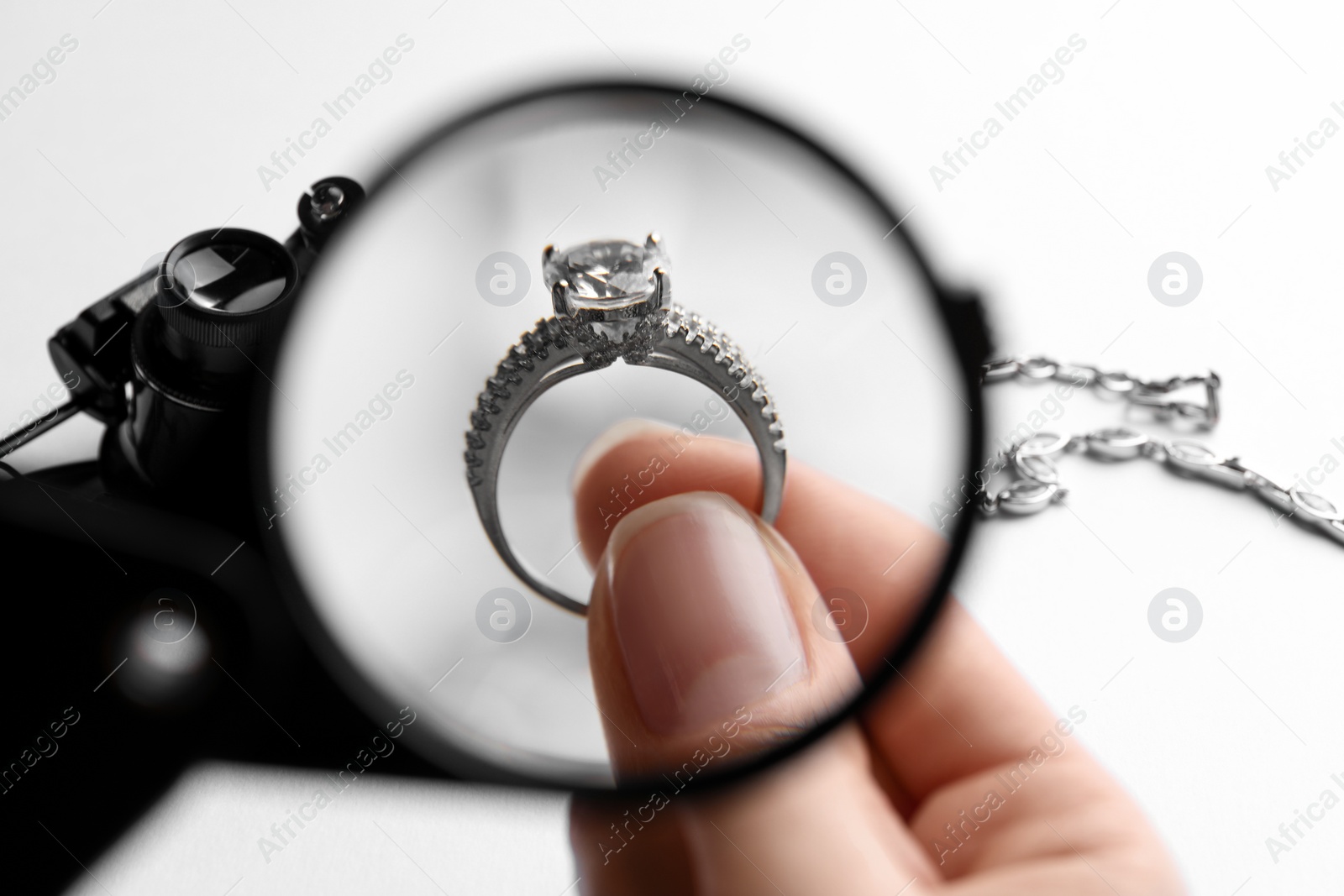 Photo of Jeweler examining diamond ring with magnifying glass at white table, closeup