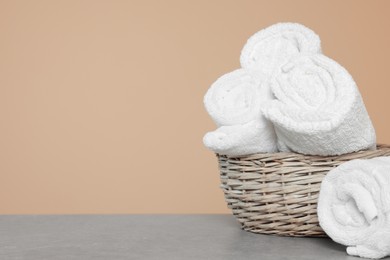 Photo of Soft rolled towels in wicker basket on grey table, space for text