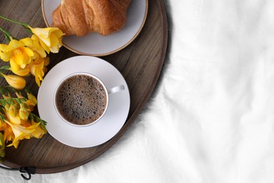 Morning coffee, croissant and flowers on bed, top view. Space for text