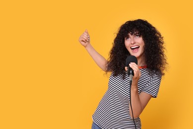 Beautiful young woman with microphone singing on yellow background. Space for text
