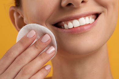 Photo of Smiling woman removing makeup with cotton pad on yellow background, closeup