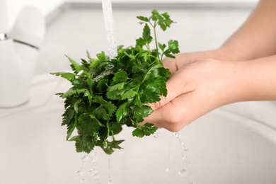 Photo of Woman washing bunch of fresh parsley under tap water in kitchen sink, closeup