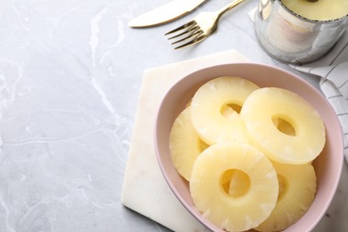 Photo of Delicious canned pineapple in bowl on light grey marble table, above view. Space for text