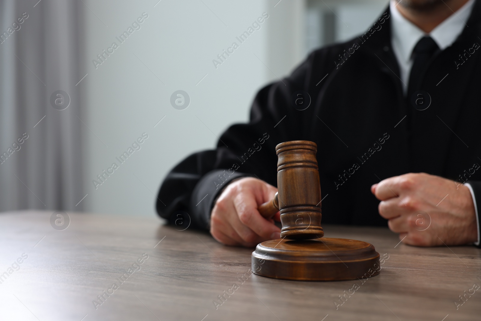 Photo of Judge with gavel sitting at wooden table indoors, closeup. Space for text