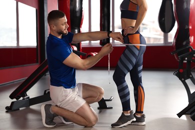 Photo of Trainer measuring woman`s hips with tape in gym