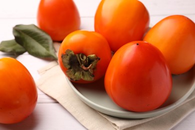 Delicious ripe juicy persimmons on white wooden table, closeup