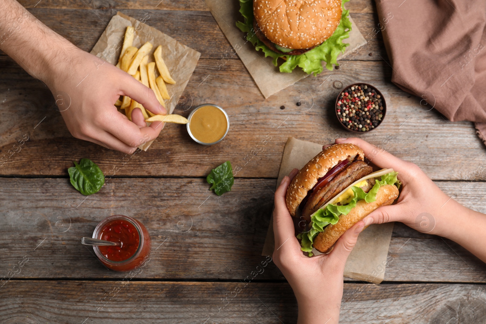 Photo of People with burger and French fries at wooden table, top view