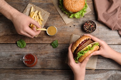Photo of People with burger and French fries at wooden table, top view