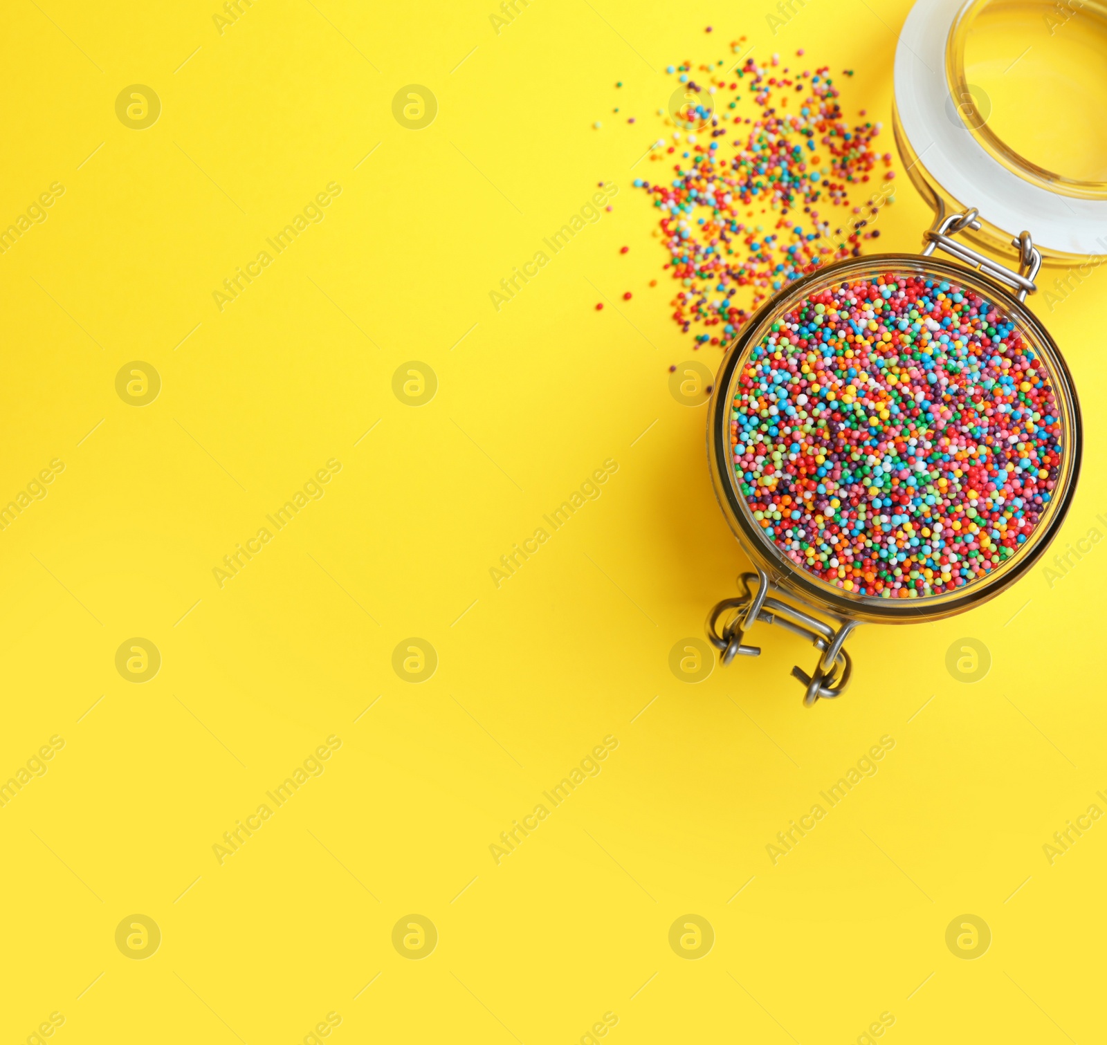 Photo of Colorful sprinkles in jar on yellow background, flat lay with space for text. Confectionery decor