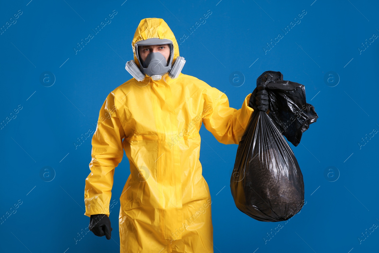 Photo of Man in chemical protective suit holding trash bag on blue background. Virus research