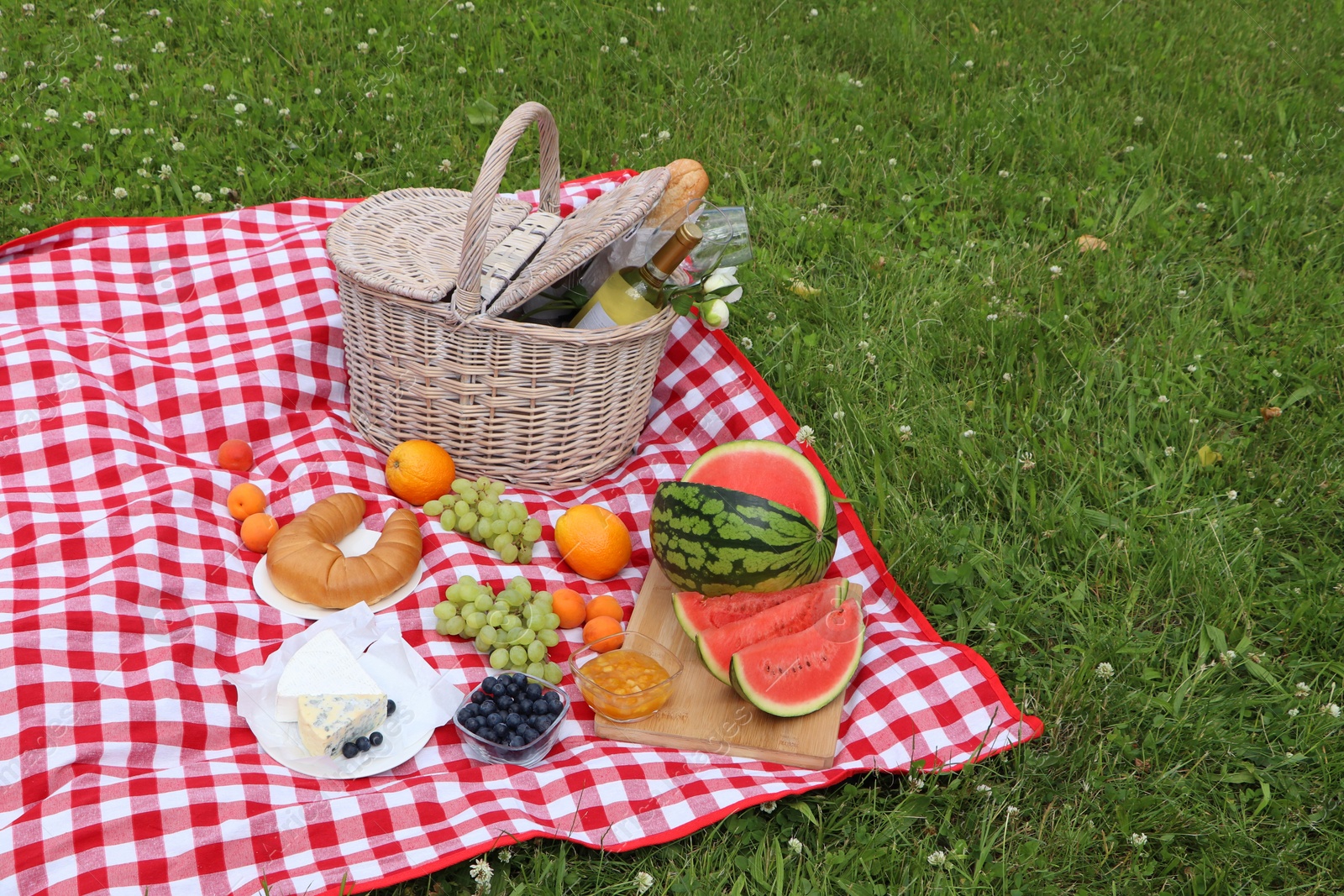 Photo of Picnic blanket with delicious food and wine outdoors on summer day, space for text