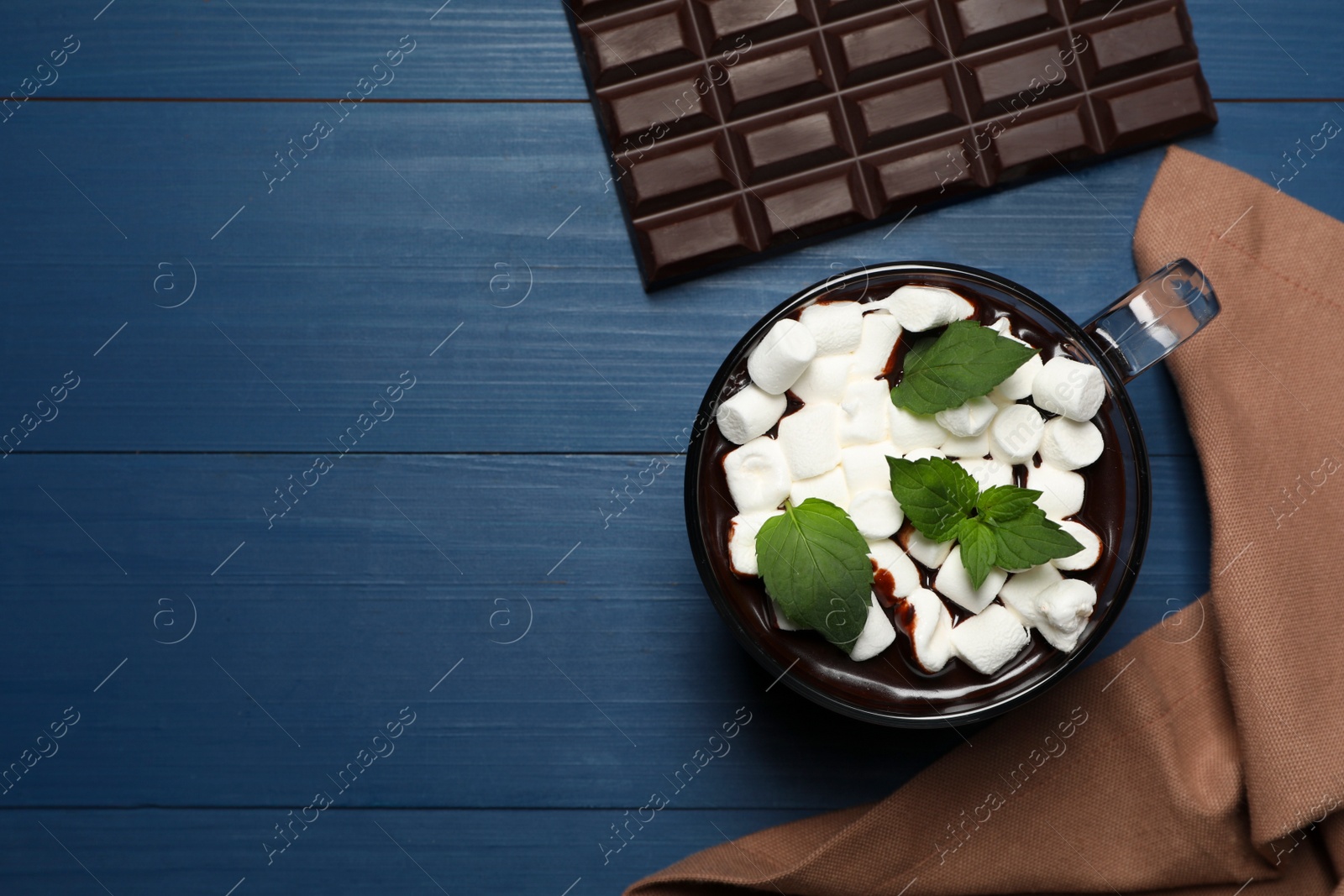 Photo of Glass cup of delicious hot chocolate with marshmallows and fresh mint on blue wooden table, flat lay. Space for text