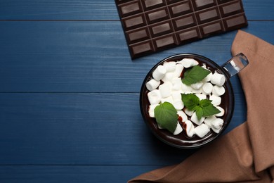 Glass cup of delicious hot chocolate with marshmallows and fresh mint on blue wooden table, flat lay. Space for text