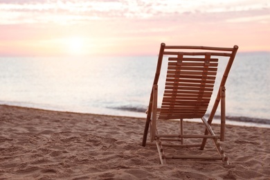 Wooden deck chair on sandy beach at sunset. Summer vacation