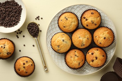 Delicious sweet muffins with chocolate chips on beige wooden table, flat lay