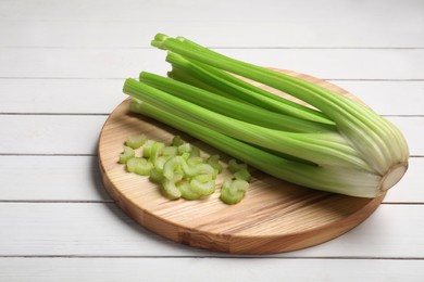 Photo of Board with fresh cut and whole celery on white wooden table, space for text