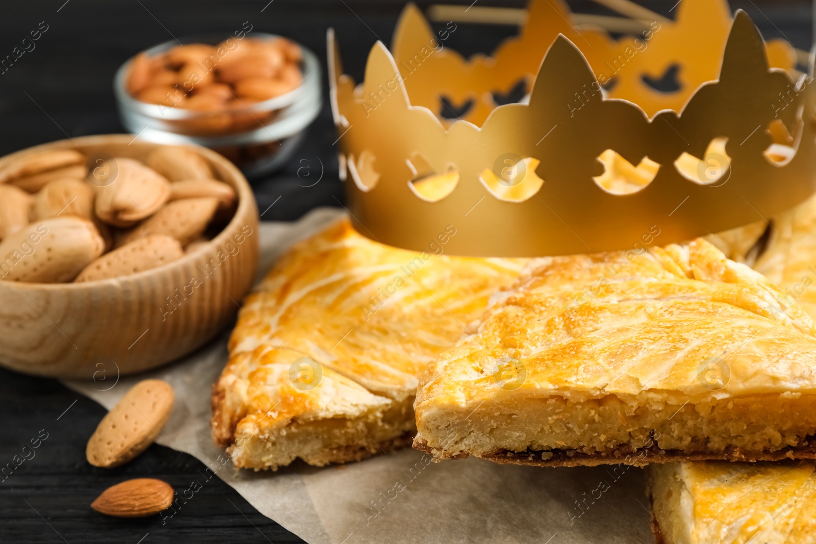 Photo of Traditional galette des Rois with paper crown on black wooden table, closeup