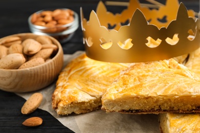 Traditional galette des Rois with paper crown on black wooden table, closeup