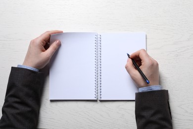 Photo of Man writing in notebook with pen at white wooden table, top view