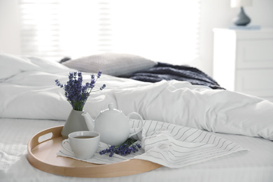 Photo of Wooden tray with cup of fresh hot tea and beautiful lavender flowers on bed, space for text. Tasty breakfast