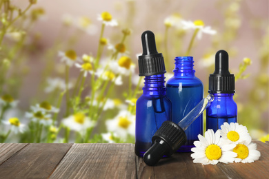 Image of Bottles of essential oil and flowers on wooden table against blurred background. Space for text