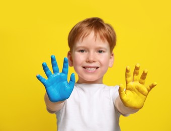 Photo of Little boy with hands painted in Ukrainian flag colors against yellow background, focus on palms. Love Ukraine concept