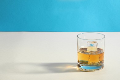 Whiskey with ice cubes in glass on white table against light blue background, space for text