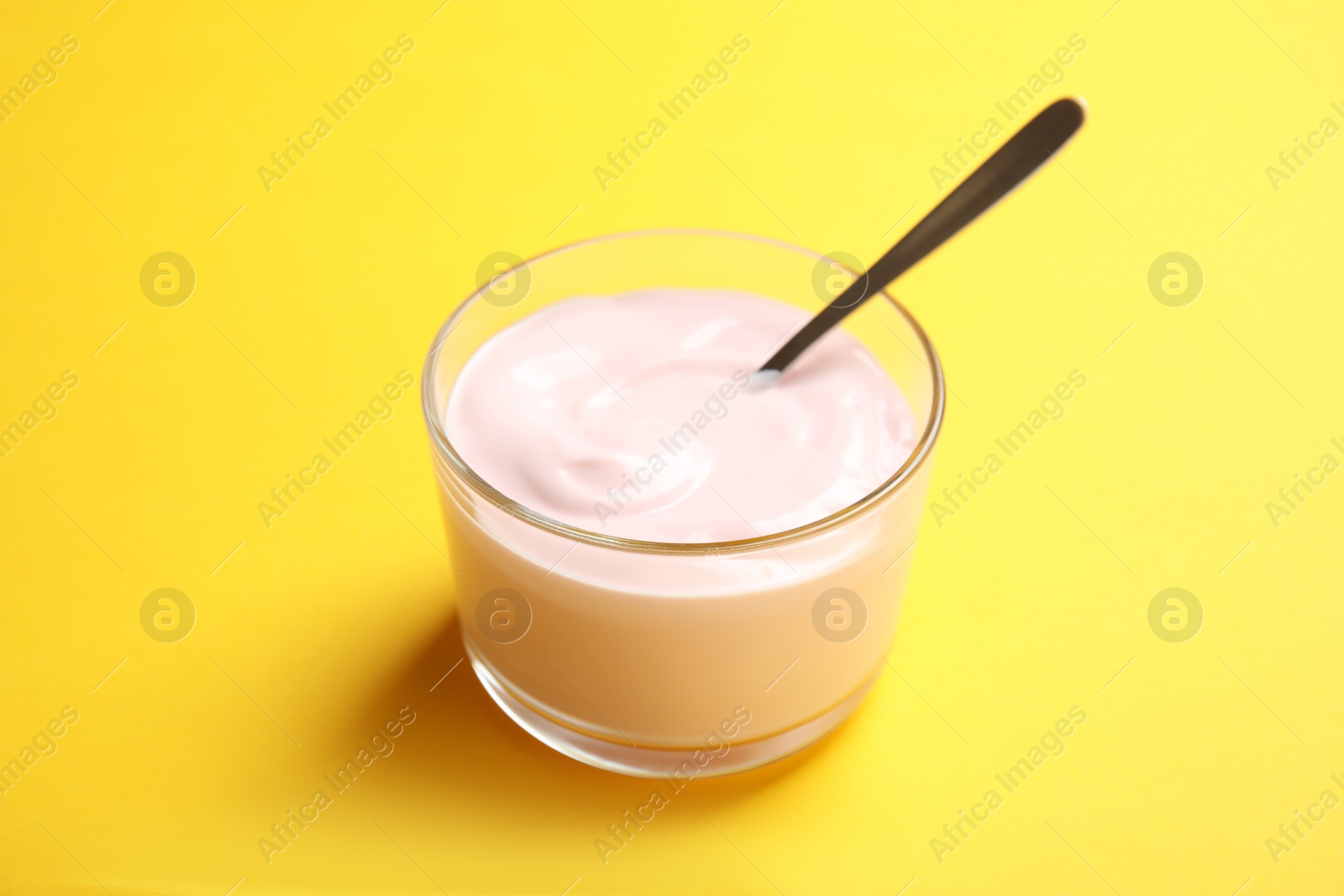 Photo of Glass bowl with creamy yogurt and spoon on color background